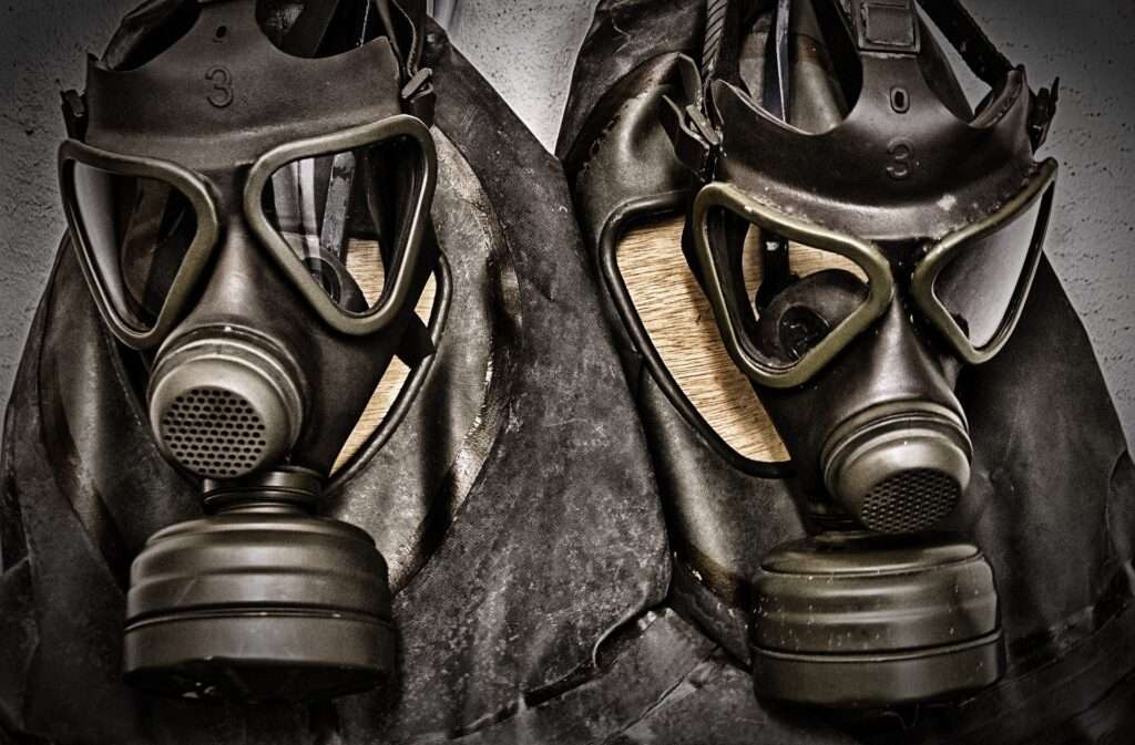 Two gas masks with black googles and black leather arranged in a row lying on a surface.