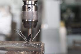 Close-up of the bits of a drill as it is pushing a nail into a wood board.