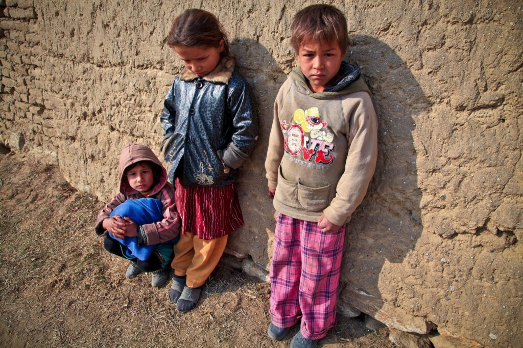 3 children in Afghanistan, The leftmost child is crouching against a wall in the sun while the others are standing